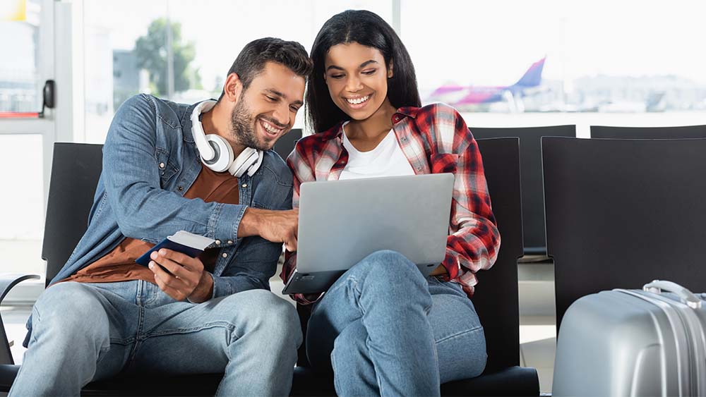 High-Yield-Airport-Couple Happy young couple sitting in an airport looking at a laptop