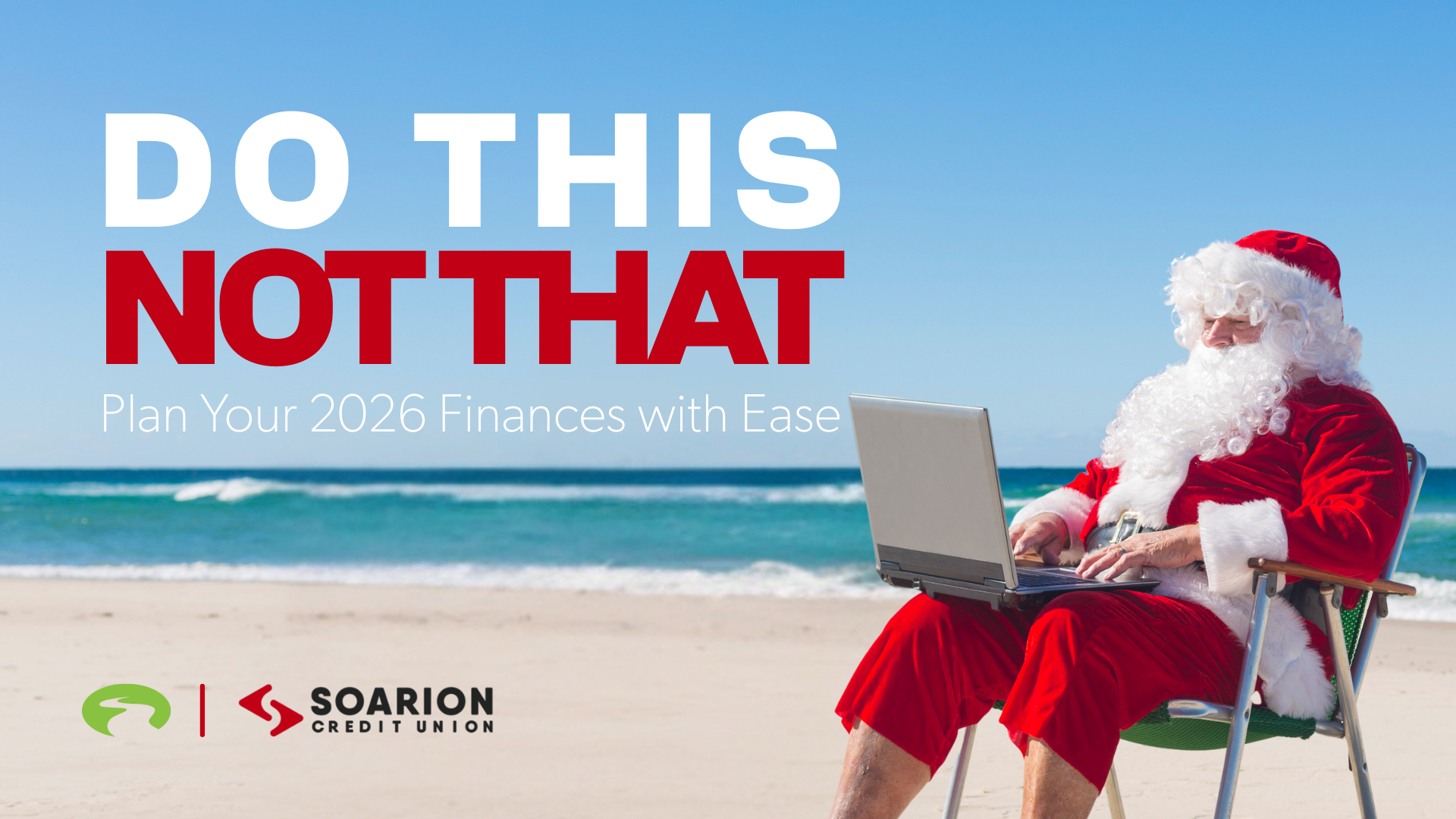 Man in a santa suit sitting in a chair on the beach looking at a laptop