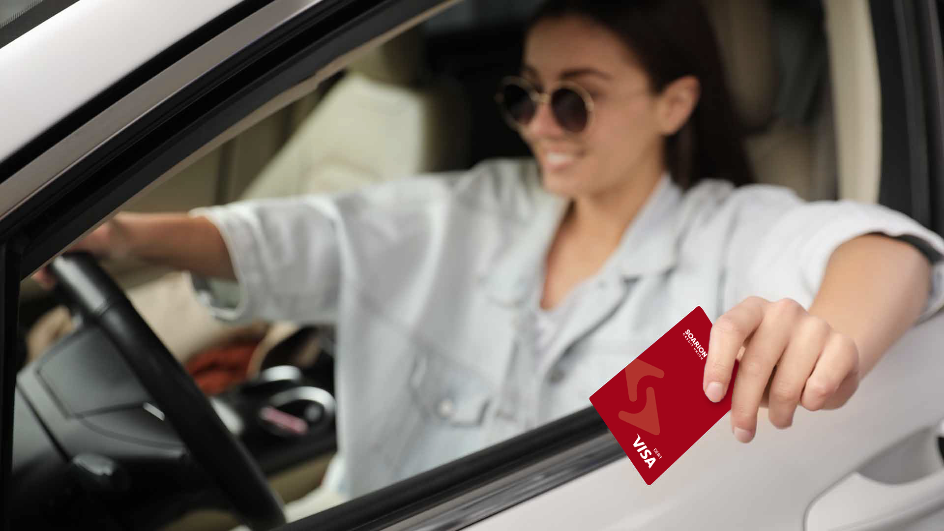 woman in driver's seat of car holding a debit card