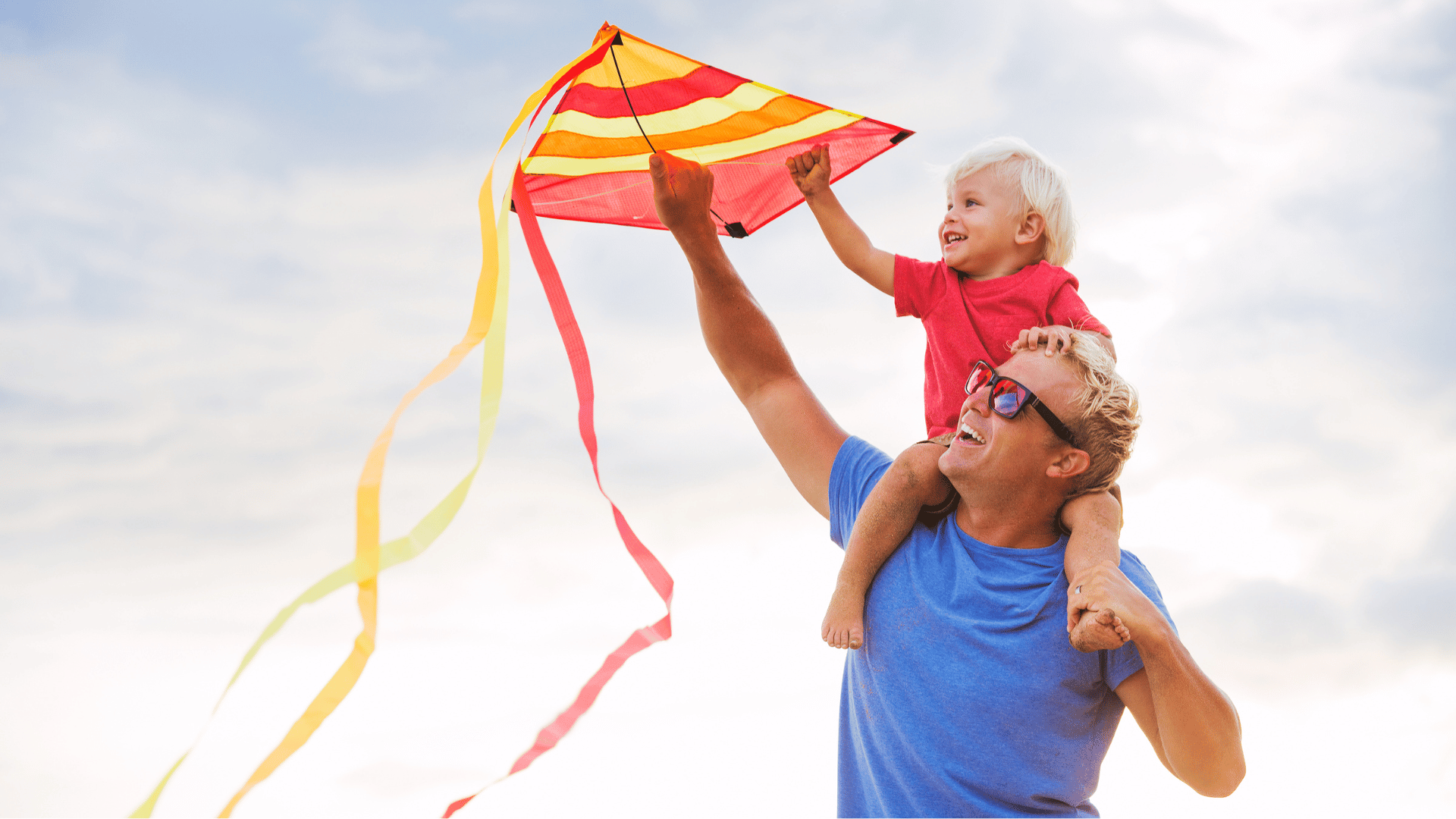 Man with child on his shoulders flying a kite