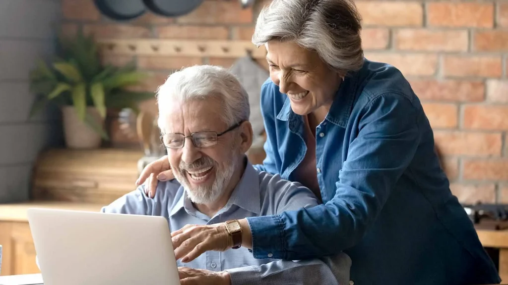 Older couple laughing together while looking at a laptop at home