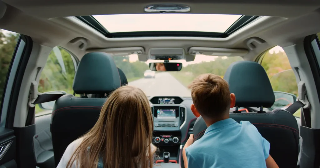 Two children riding in the backseat of a car on a sunny road