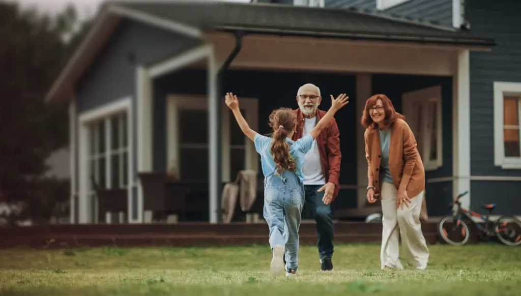 Young girl running across a lawn toward her grandparents in front of a home