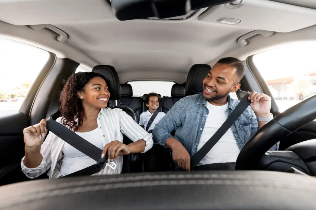 Family smiling and fastening seatbelts inside a car
