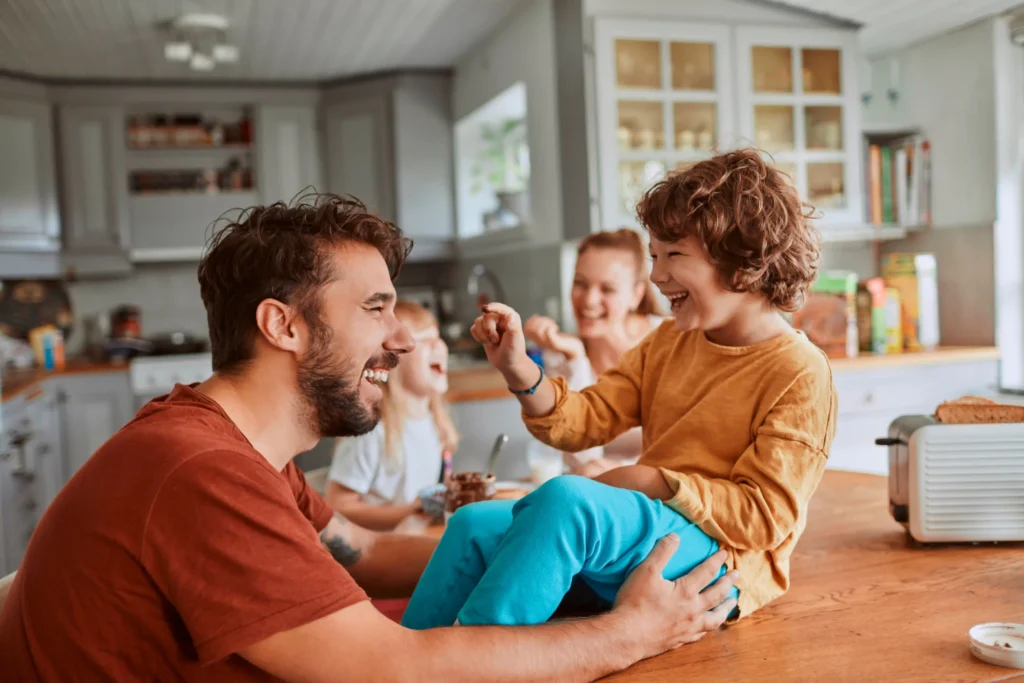 Family laughing together in a kitchen with a child sitting on the counter