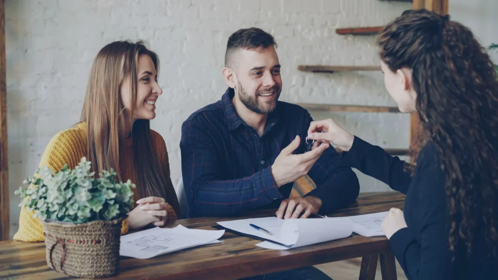 hand passing house keys to a new homeowner with a smiling couple in the background