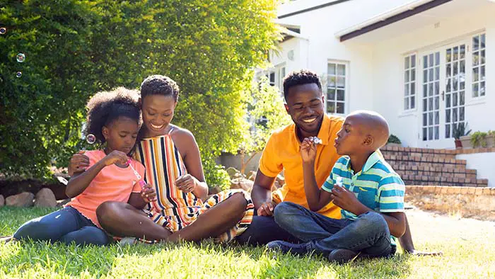 Family blowing bubbles on the lawn in front of a suburban home