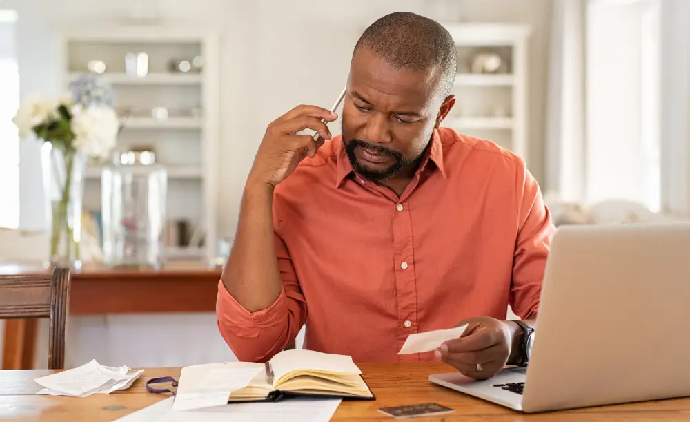Man on the phone while reviewing a card and paperwork at a desk