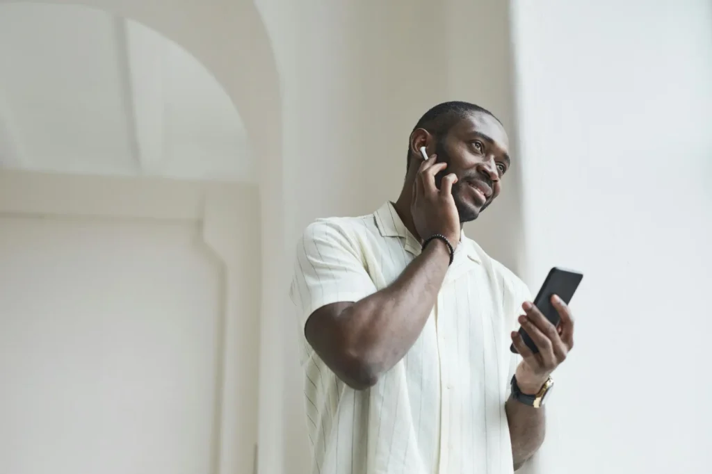 Man smiling while holding a smartphone and wearing wireless earbuds