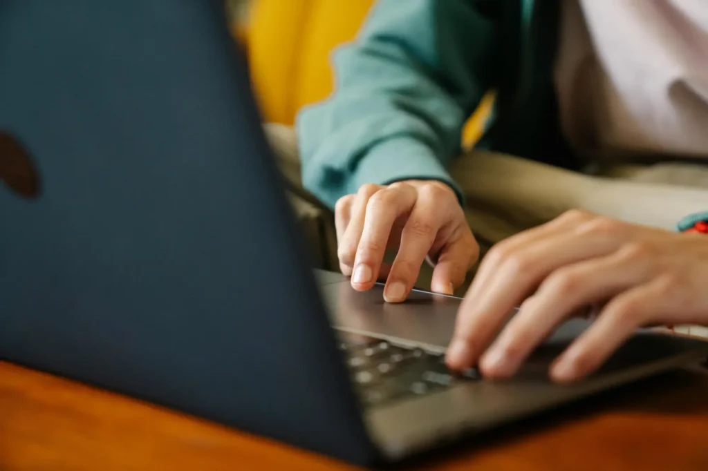 Hands typing on a laptop keyboard on a wooden desk