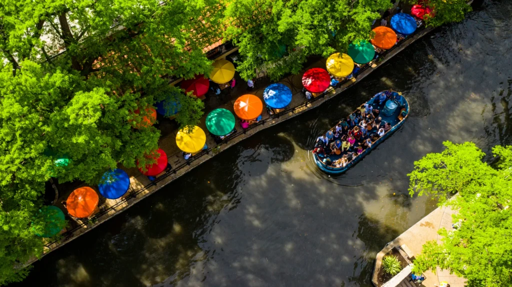 Aerial view of a riverwalk with a tour boat and colorful umbrellas along the walkway