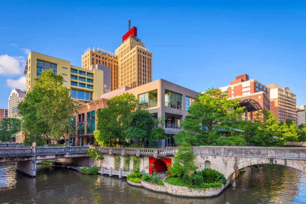 City riverfront at dusk with a bridge, trees, and downtown buildings